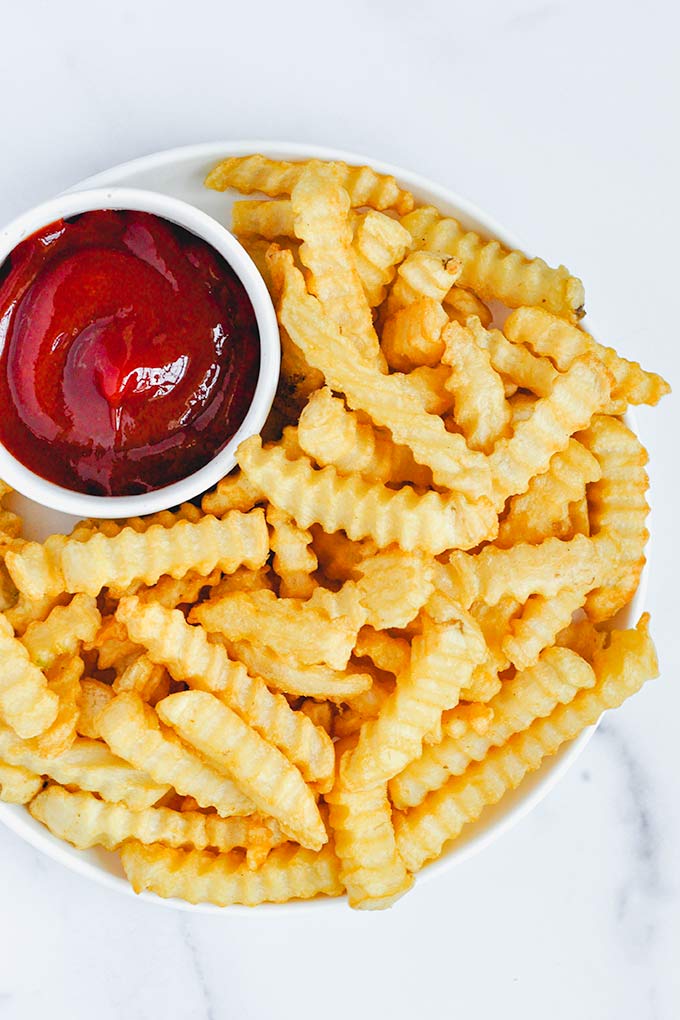 A plate of crinkle fries with a cup of ketchup.