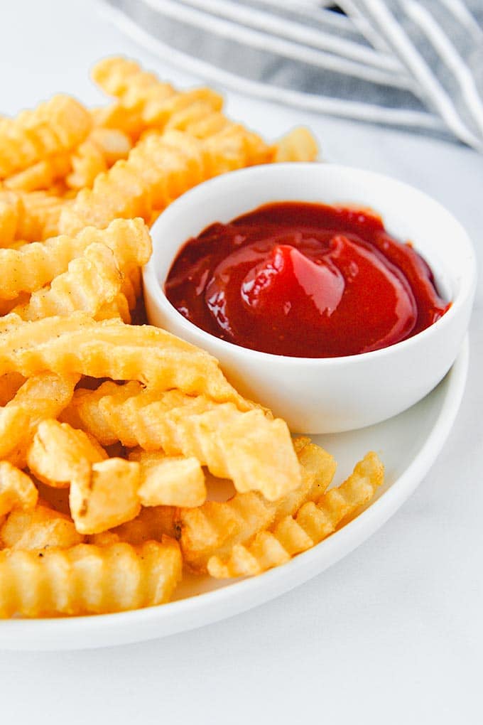 A plate of crinkle fries with a cup of ketchup.