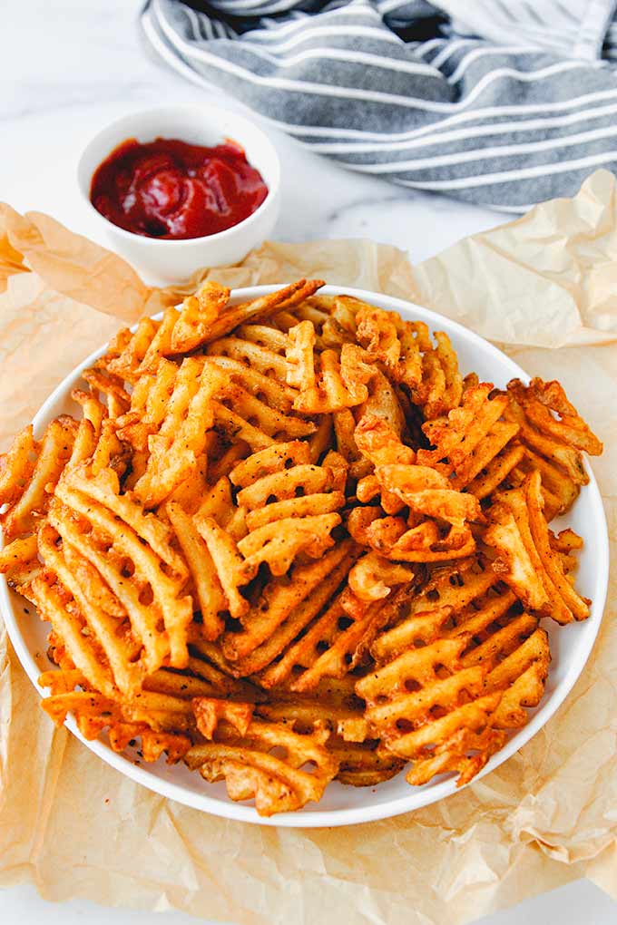 A plate of waffle fries with a cup of ketchup.