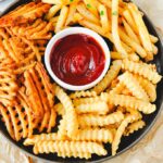 Straight, waffle, and crinkle fries on a platter with ketchup.