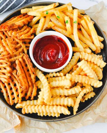 Straight, waffle, and crinkle fries on a platter with ketchup.