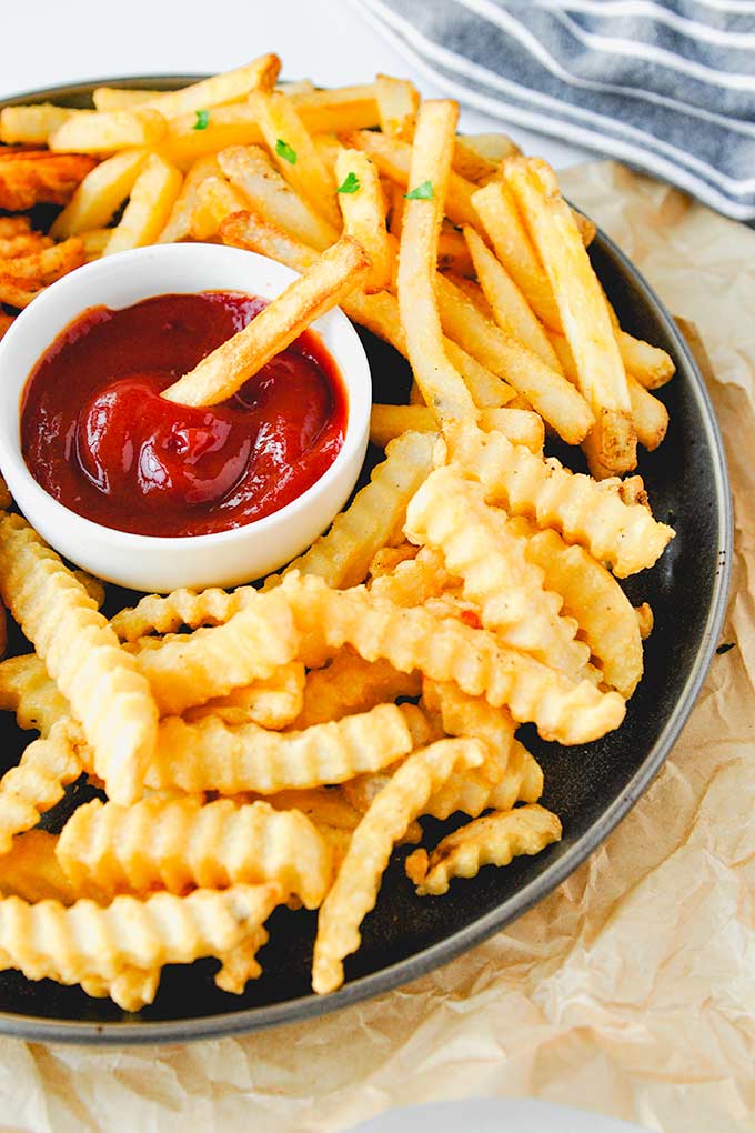A tray of waffle fries, crinkle fries, and straight fries with a cup of ketchup.
