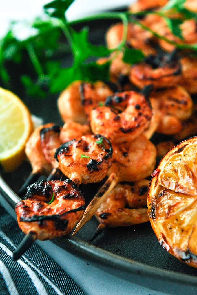 Grilled shrimp on skewers with lemon slices, parsley, and a striped towel.