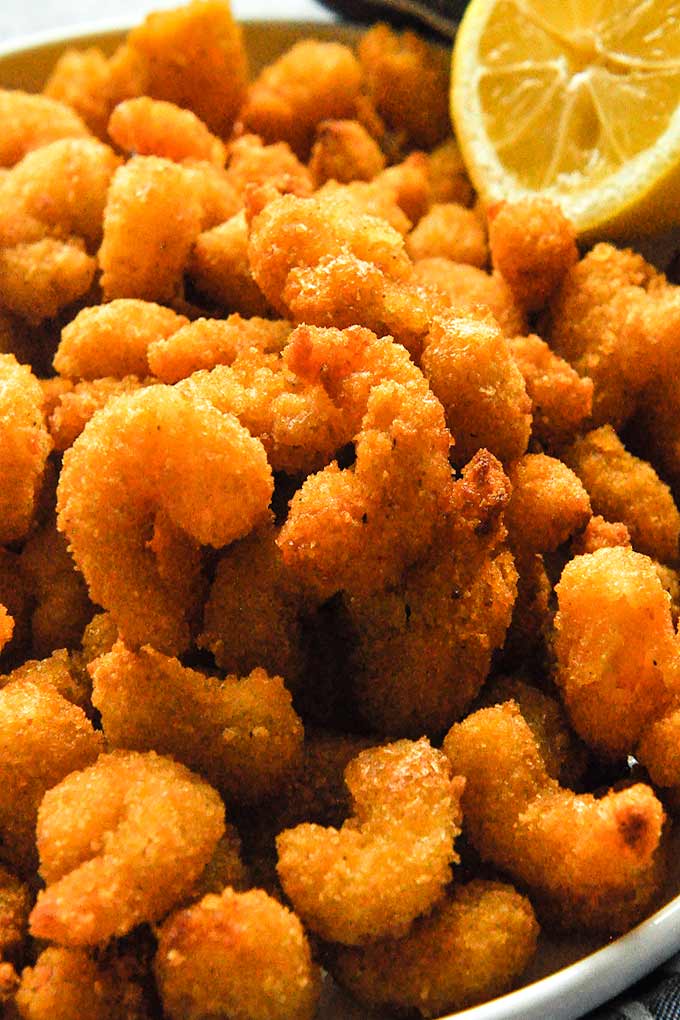 A closeup of all the fried shrimp served with a lemon.