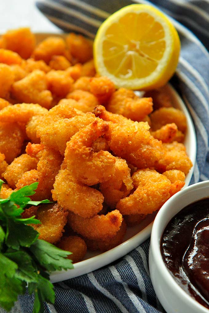 A plate full of fried shrimp with sauce and a lemon in the background.