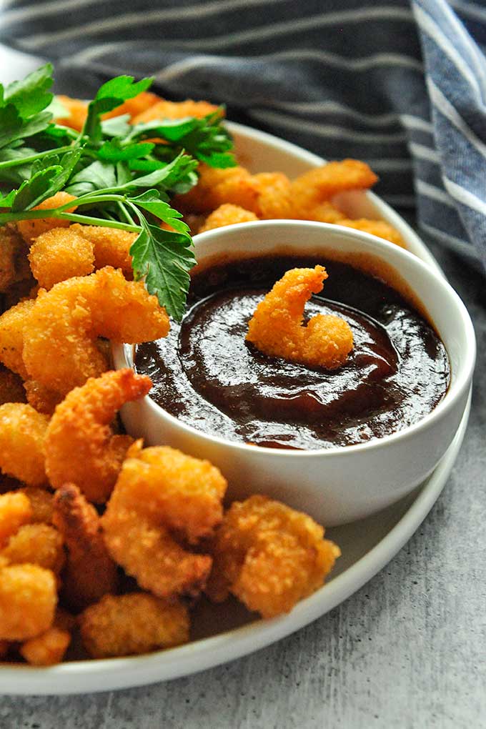 A plate full of fried shrimp with a single shrimp in the dipping sauce.