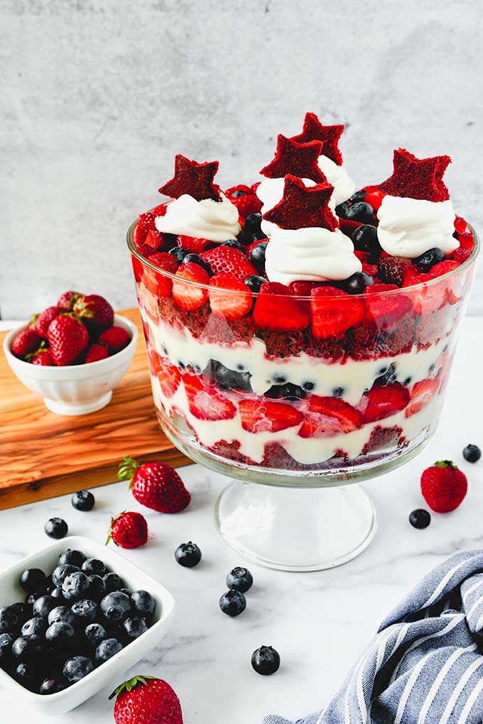 Whole assembled trifle with whipped cream and cake stars on top, strawberries and blueberries around.
