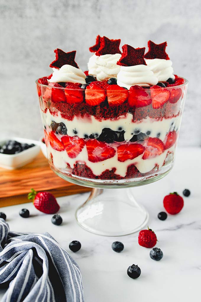 Whole assembled trifle with whipped cream and cake stars on top, strawberries and blueberries around.