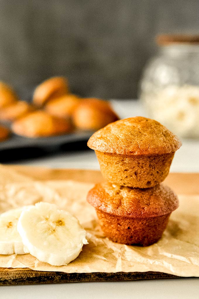 Two mini banana muffins stacked on top of each other next to some banana slices.