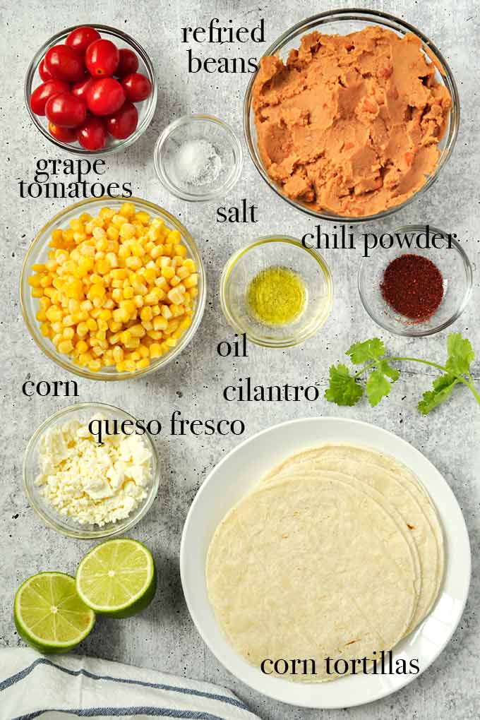 All of the ingredients needed for bean tostadas like corn, chili powder, corn tortillas, and tomatoes.