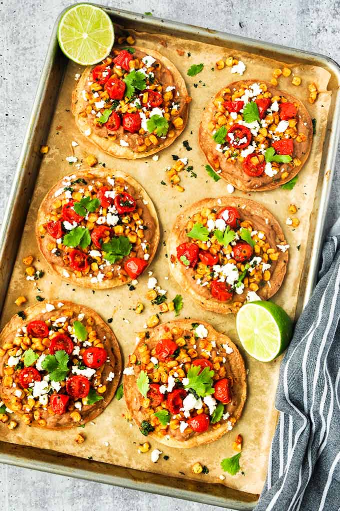 An above view of six tostadas on a baking tray with limes.