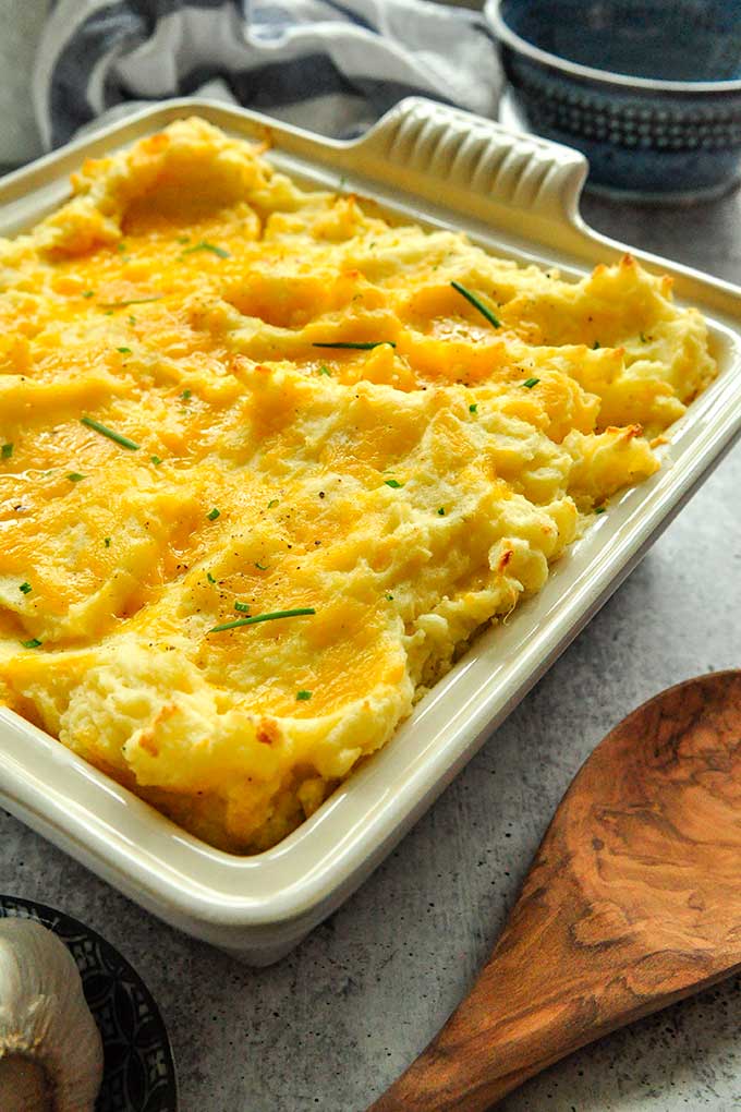 Cheesy garlic mashed potatoes in a baking dish topped with garlic chives.