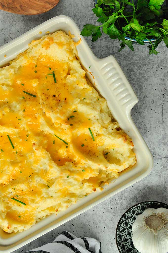 Above view of cheesy garlic mashed potatoes in a baking dish topped with garlic chives.