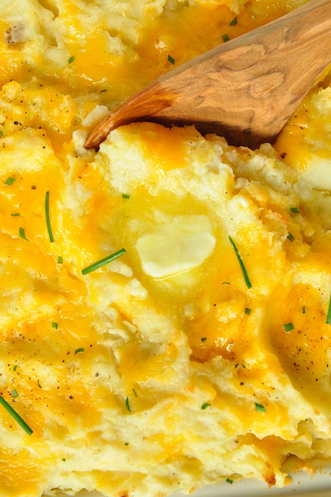 Very up close view of cheesy mashed potatoes topped with a pat of butter and chives.