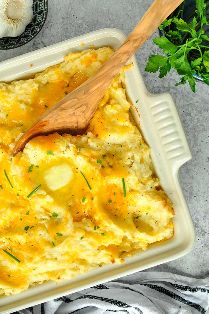 heesy garlic mashed potatoes in a baking dish topped with garlic chives.
