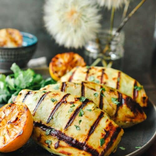A plate with greek yogurt chicken breast served with lemon halves and cilantro