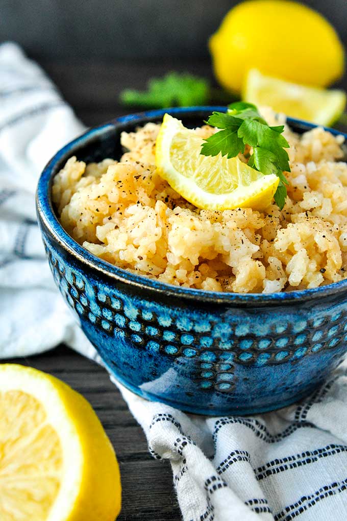 A blue bowl filled with lemon butter rice, topped with a lemon wedge and parsley.