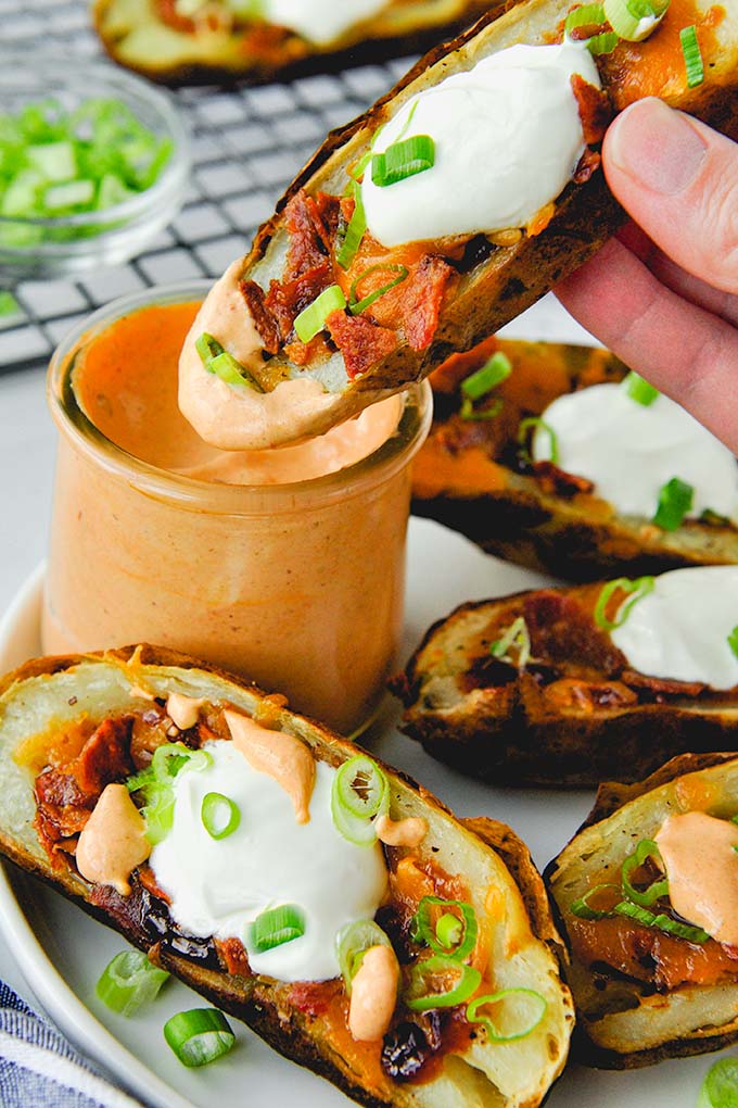 Air fryer potato skins topped with sour cream and green onions on a plate and a jar of chipotle mayonnaise with a potato skin being dunked in.
