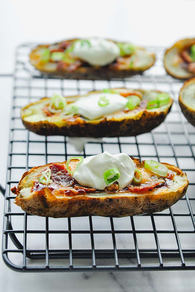 Air fried potato skins lined up on a cooking rack topped with sour cream and green onions.
