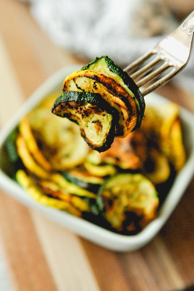 A forkful of squash with a bowl of zucchini and yellow squash that has been air fried in the background.