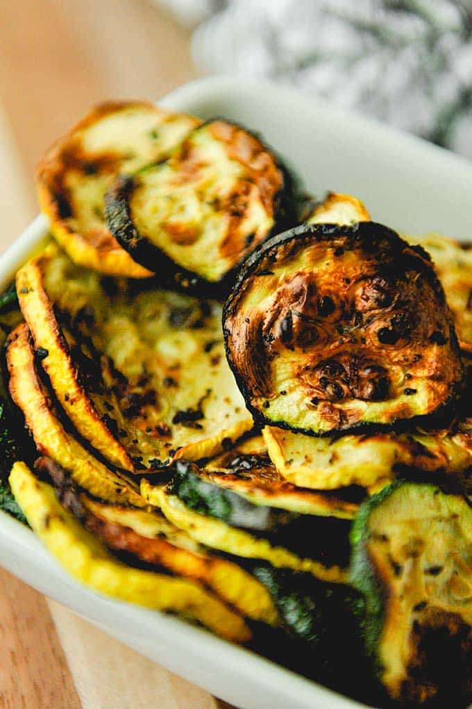 A close up of a bowl of air fryer squash and zucchini with a towel in the background.