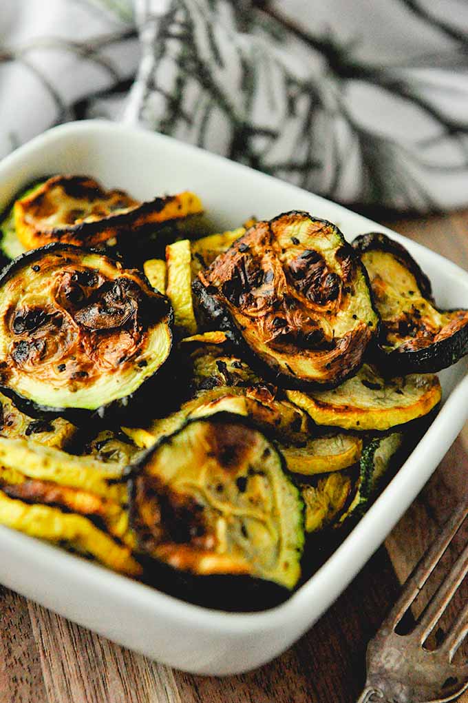 A bowl of air fryer squash and zucchini with a fork and towel in the background.