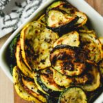A bowl of air fryer squash and zucchini with towel in the background.