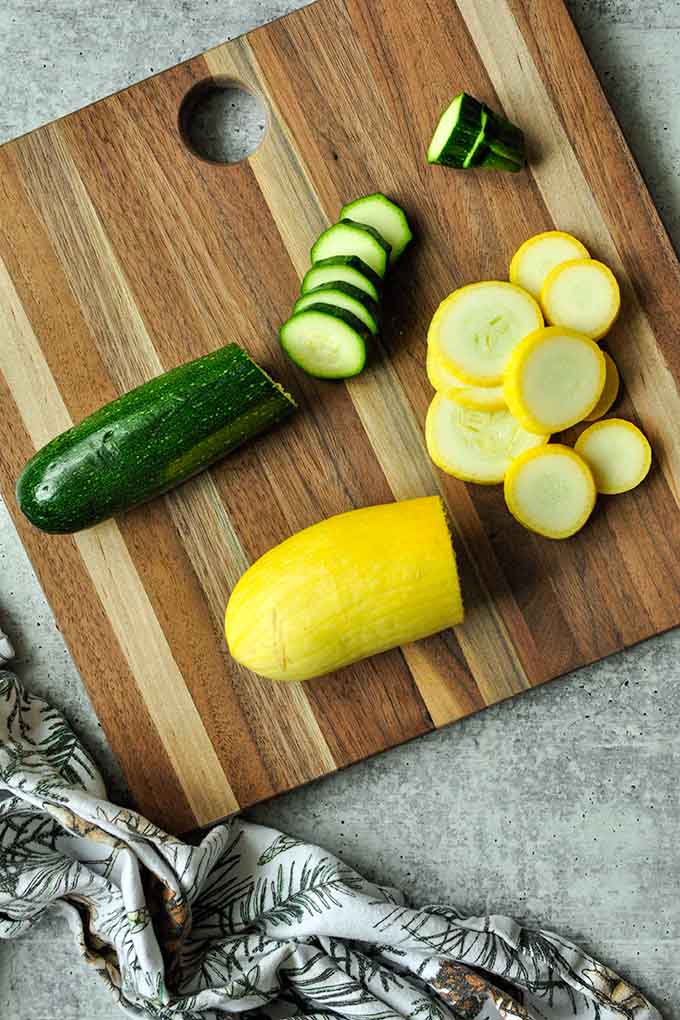 A zucchini and yellow squash being sliced on a cutting board.