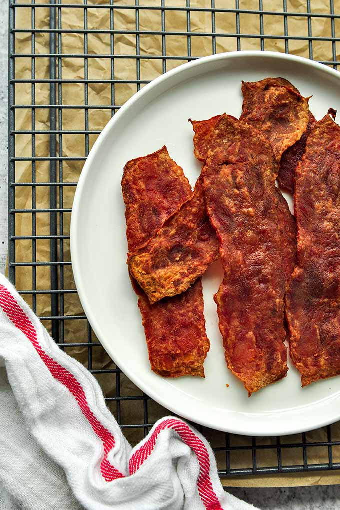 A plate of crisp turkey bacon on a cooling rack with a red striped towel.