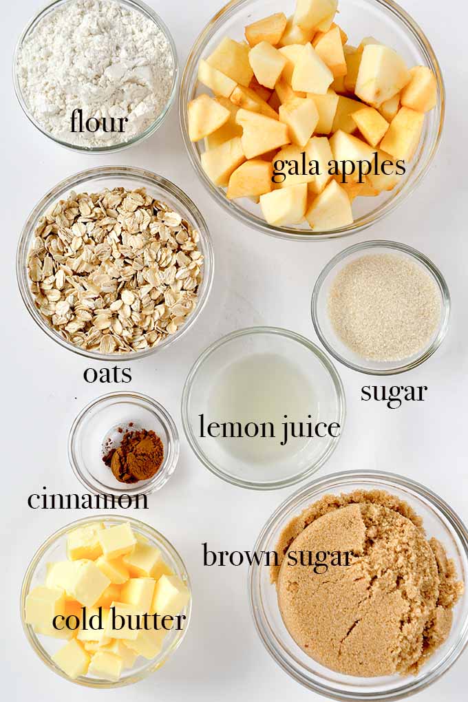 All of the ingredients needed to make apple crisp such as oats, cinnamon, cubed butter, and apples.