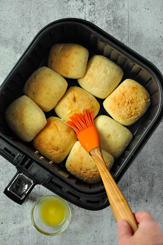 An air fryer with 9 frozen rolls with butter being spread on top.