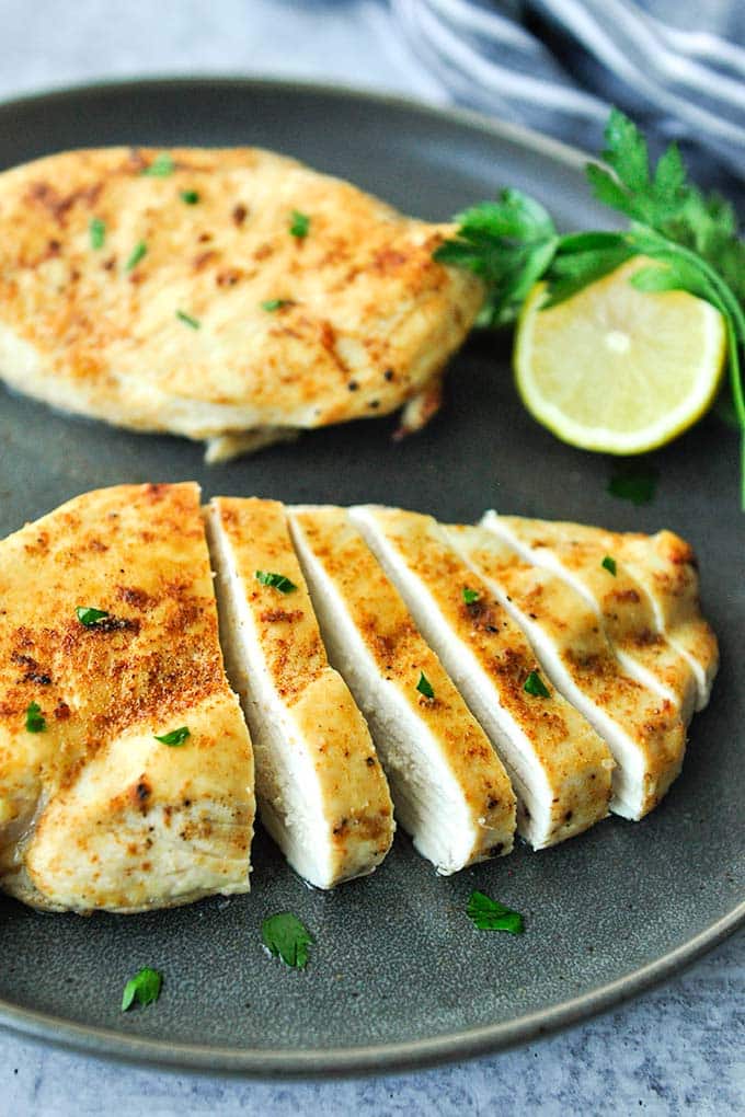 Two cooked pieces of air fryer chicken breast with no breading, one breast is cut into cutlets.