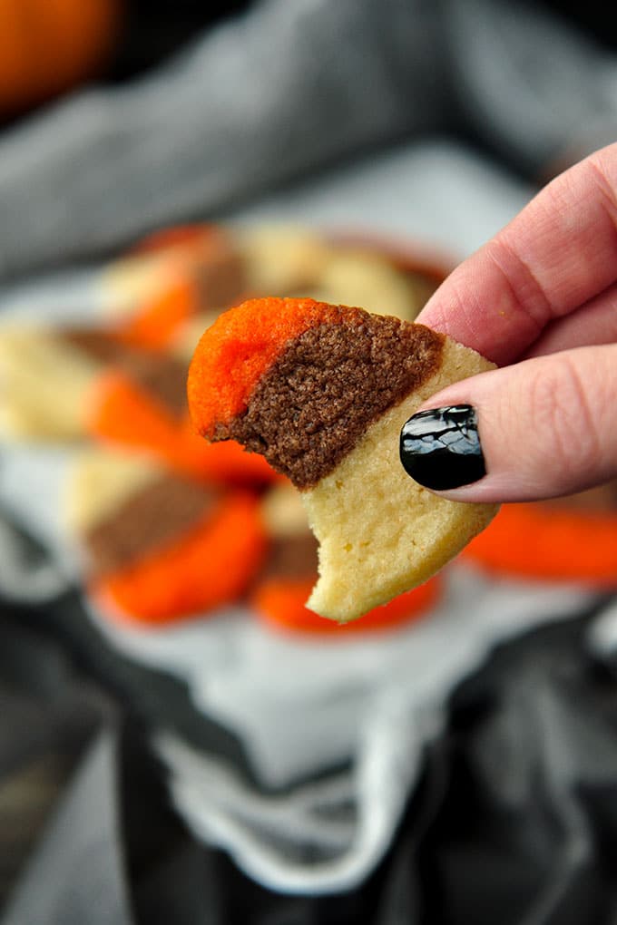 A close up of a candy corn cookie with a bite taken out of it, being held by a hand with black painted nails.