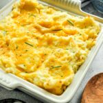 Cheesy garlic mashed potatoes in a baking dish topped with garlic chives.