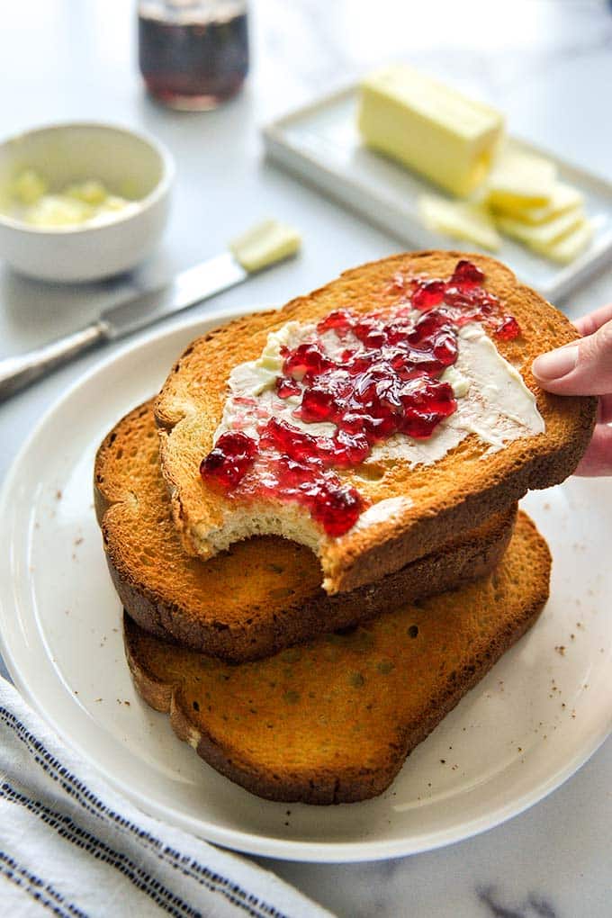 A hand reaching into a stack of buttered and jelly toast on a plate.