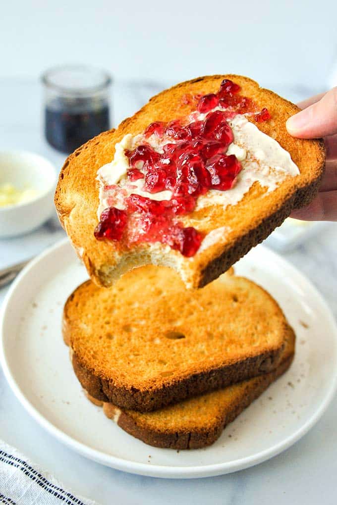 A piece of jelly and buttered toast with a bite missing being held.