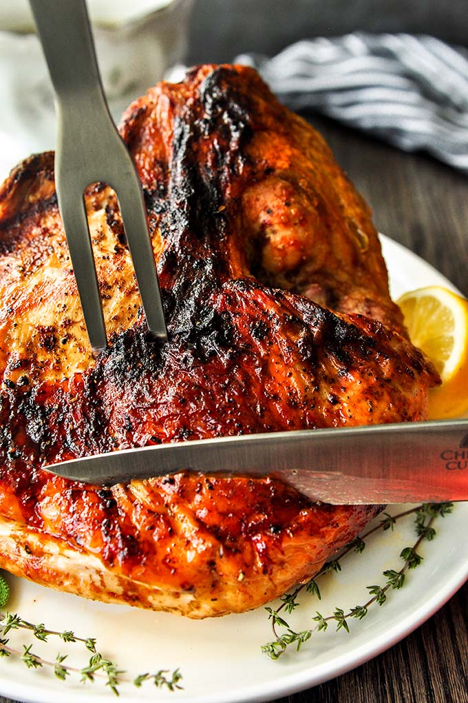 Air Fryer Turkey Breast on a platter being held in place with a meat fork and cut with a knife. 
