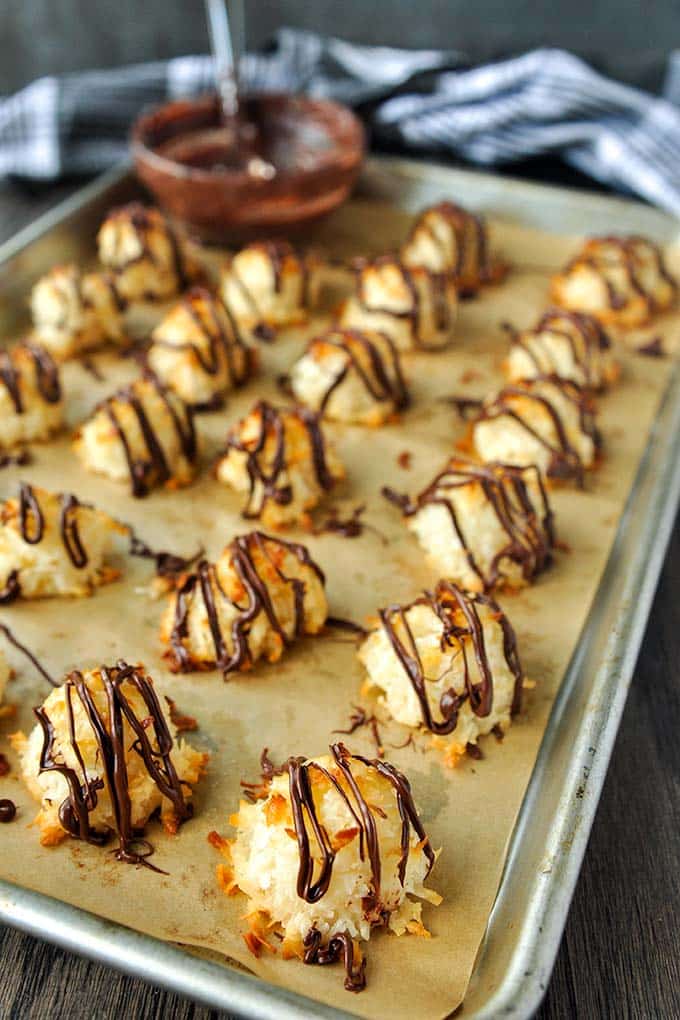 A baking sheet of baked coconut macaroons with condensed milk drizzled with melted chocolate.