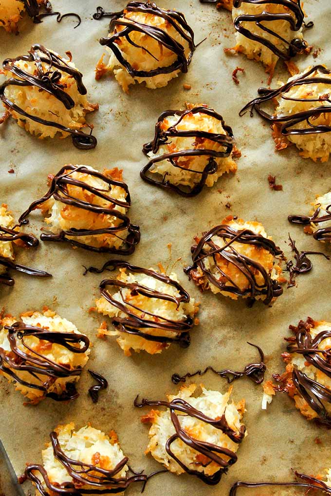 A baking sheet of baked coconut macaroons with condensed milk drizzled with melted chocolate.