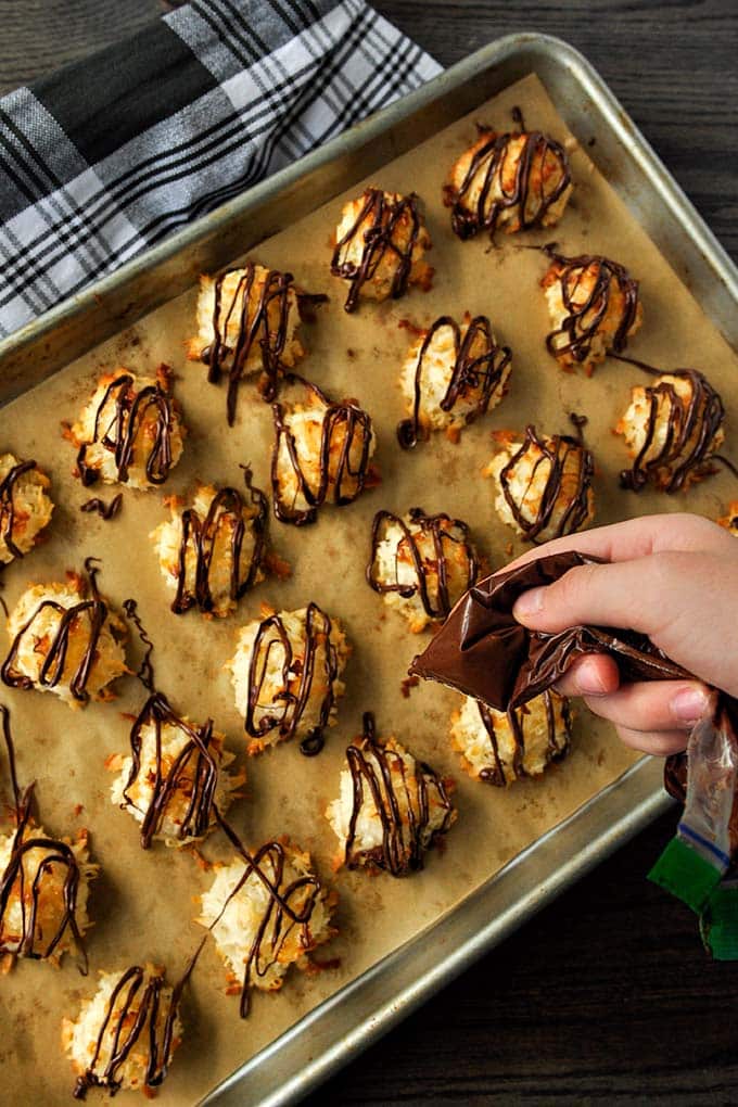 A baking sheet of baked coconut macaroons with condensed milk and melted chocolate being drizzled on.