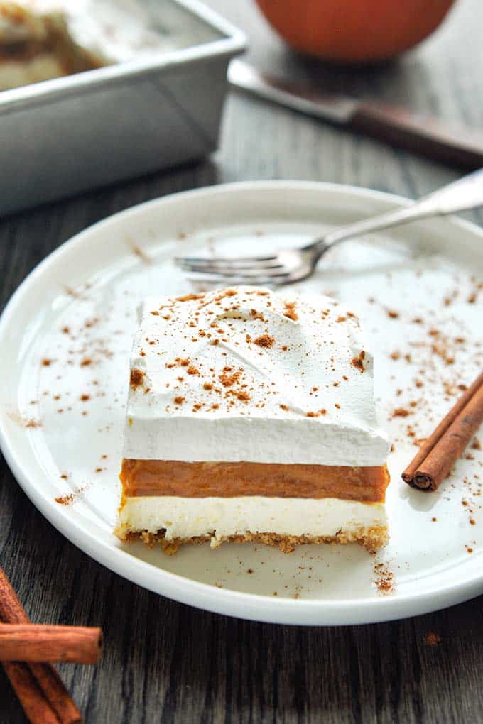 A square of no bake pumpkin pie cheesecake on a plate with cinnamon sticks.