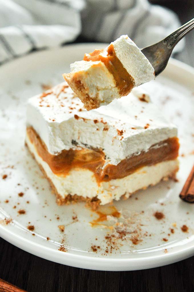 A square of no bake pumpkin pie cheesecake on a plate with a big bite on a fork.