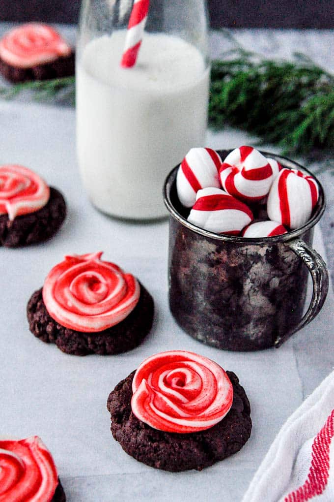 Frosted peppermint brownie cookies next to a metal cup of peppermints and a bottle of milk.