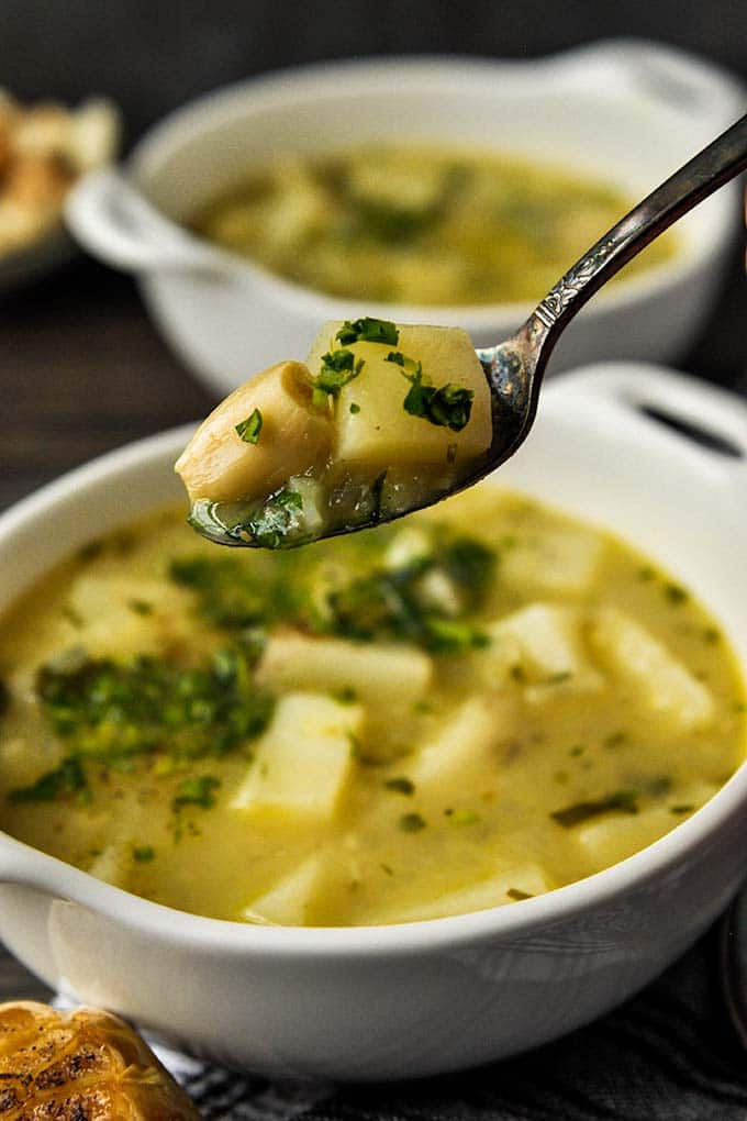 A spoon of garlic potato soup above a bowl of the soup.