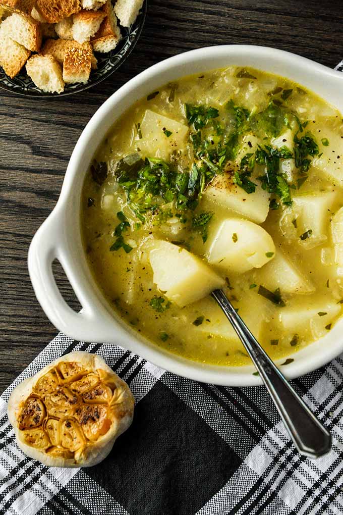 An up close of a bowl of garlic potato soup with croutons, fresh parsley, and roasted garlic.