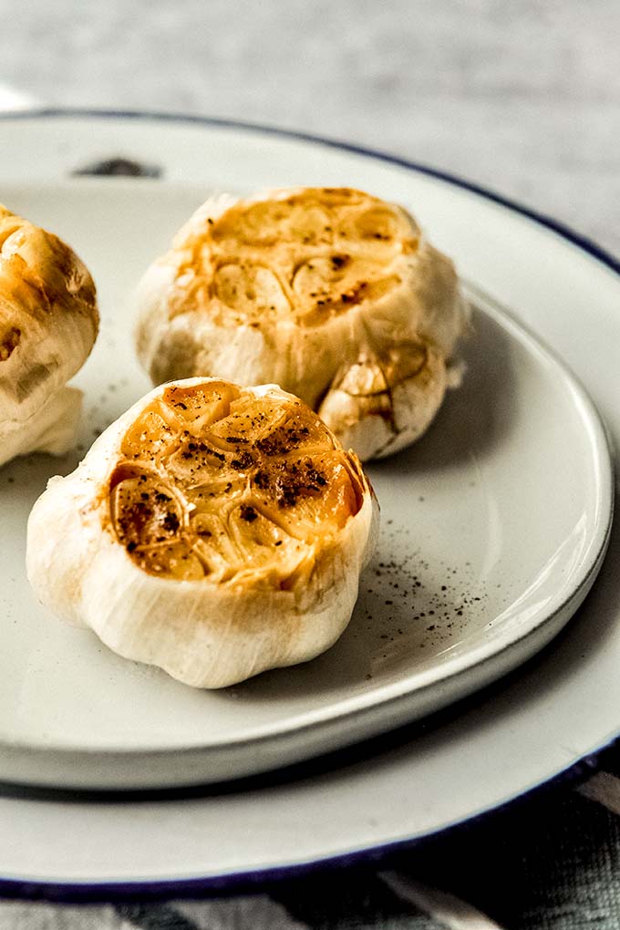 Close up of two roasted garlic in Air Fryer sprinkles with salt and pepper on a plate.