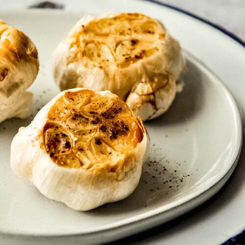 Close up of two roasted garlic in Air Fryer sprinkles with salt and pepper on a plate.