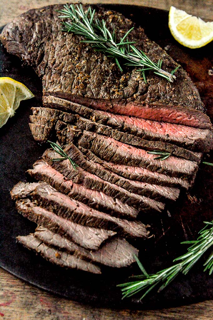 Air fryer London Broil sliced on a platter with cut lemons and rosemary.