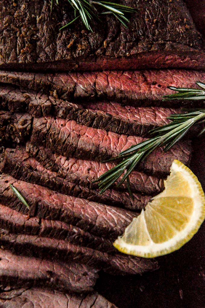 Up close of air fried London Broil with a sprig of rosemary and a lemon wedge.