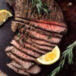 Air fryer London Broil sliced on a platter with cut lemons and rosemary.